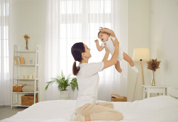 Mother and little child playing and having fun together. Happy mom sitting on the bed at home and...