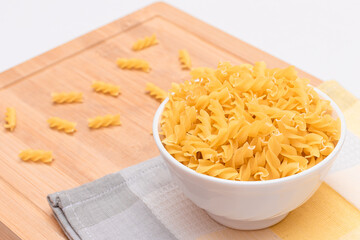 Uncooked Fusilli Pasta in White Bowl on Wooden Board. Raw and Dry Macaroni. Unhealthy and Fat Food. Italian Culture