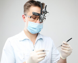 Young dentist male in white lab coat and mask holding dental instruments