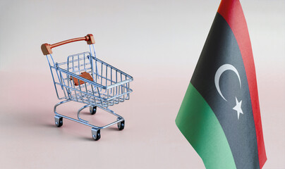 An empty metal shopping basket and the flag of the State of Libya on a light background is a...
