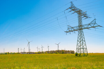 Beautiful farm landscape with meadow at blossom field, wind turbines to produce green energy and high voltage power lines in Germany, at Spring and blue sunset sky.