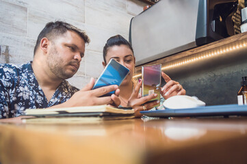 young latin male and female couple in restaurant, she shows her cell phone to him.