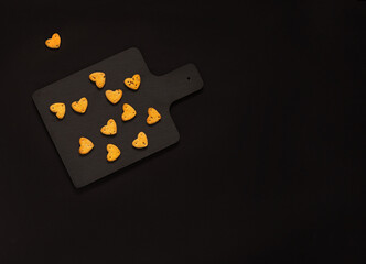heart shaped cookies on a black cutting board on a black background. Copy space