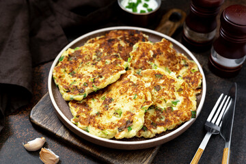 Homemade potato pancakes with cottage cheese and green onions in a ceramic plate on a dark background. A traditional dish of European cuisine from vegetables close-up	