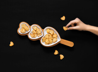 a woman's hand and  heart shaped cookies on a black background.  Copy space