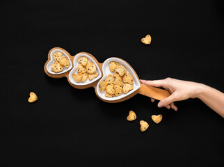 a woman's hand holds a plate of  heart shaped cookies on a black background.  Copy space