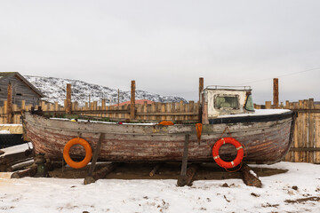 Old fishing boat on the background of a wooden fence. Teriberka village, Murmansk region, Russia.