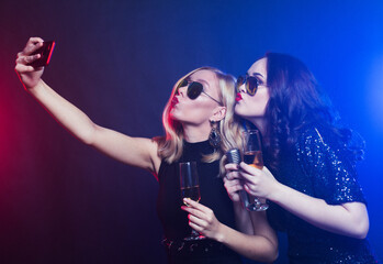 Close-up shot of group of laughing women wearing black dresses having party, take selfie with smartphone