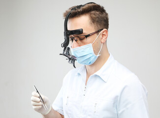 Young dentist male in white lab coat and mask holding dental instruments