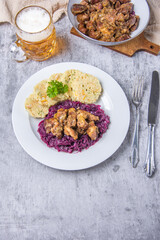 Typical Czech national meal with homemade bread dumplings red cabbage and beer on concrete texture background. Roast pork with dumplings and sauerkraut. Top view. Vertical photo.