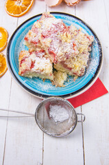Strawberry souffle cake on blue plate and wheels of dried orange, eggshells on white wooden boards. Vertical photo.
