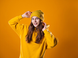 Naklejka premium Stylish cheerful young brunette in a yellow hoodie and hat on a yellow background