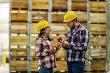 Man explains to the girl with his hands and facial expressions about the situation at work. She listens to him carefully. They are wearing a helmet. Sharing knowledge and experience in a warehouse