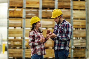 Plakat Man explains to the girl with his hands and facial expressions about the situation at work. She listens to him carefully. They are wearing a helmet. Sharing knowledge and experience in a warehouse