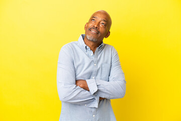 Cuban Senior isolated on yellow background looking up while smiling
