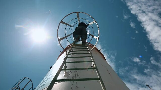 Male worker up the ladder is for inspection shell plate top of storage tank chemical.