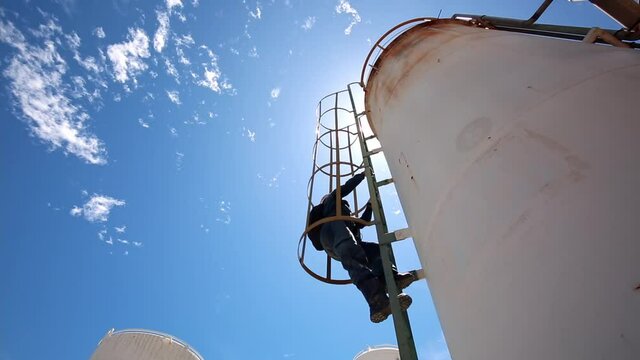 Male worker up the ladder is for inspection shell plate top of storage tank chemical.