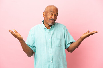 Cuban senior isolated on pink background having doubts while raising hands