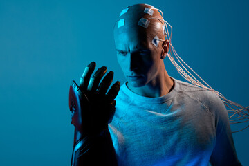 young man with a head entangled with wires and with a robotic arm, augmentations of the human body....