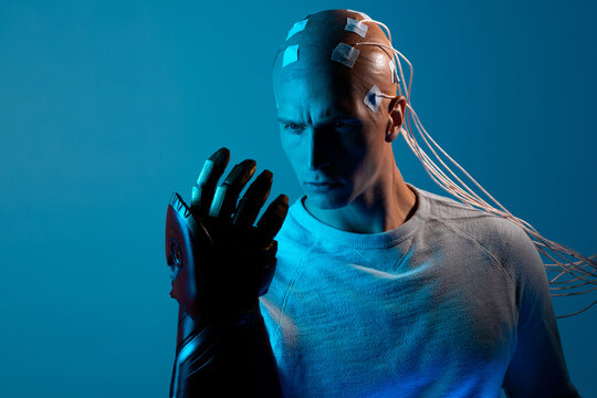 young man with a head entangled with wires and with a robotic arm, augmentations of the human body. contacts on the bald, signals to the brain. Neurointerface, future technologies, creative concept.