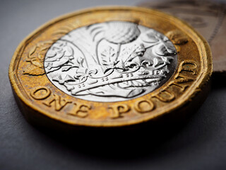 British money lies on a dark surface. 1 pound sterling coin close up. Focus on the crown. Economy and banking in England. Illustration with vignetting. Macro