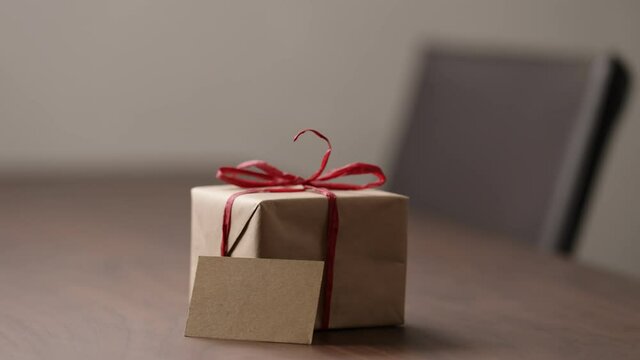 Slide tracking shot of brown paper gift box with red bow on wood table with blank paper card