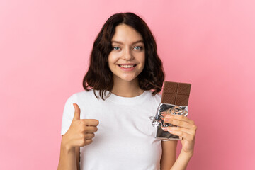 Teenager Ukrainian girl isolated on pink background taking a chocolate tablet and with thumb up