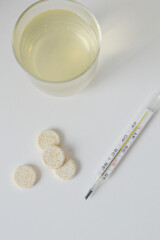 Top view of water soluble pills next to a glass thermometer showing fever symptoms