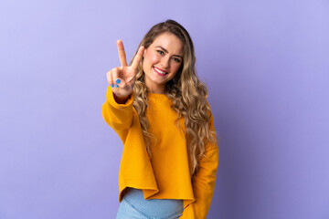 Young Brazilian woman isolated on purple background smiling and showing victory sign