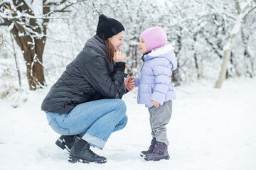 Fototapeta na wymiar Happy mom and little daughter spend time together and play. Walk in the snowy park.