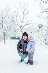 Fototapeta na wymiar Happy mom and little girl spend time together and play. Walk in the snowy park.