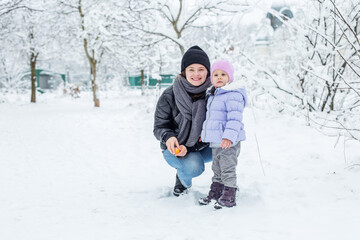 Fototapeta na wymiar Happy mom and child spend time together and play. Walk in the snowy park.
