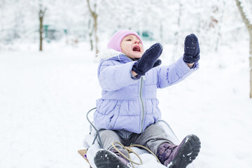 A frightened little kid is crying on a sled. Walk in the snowy park.