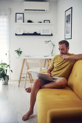 Fototapeta premium Man working on a laptop from the living room. Work from home concept.
