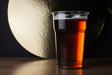Plastic glass of IPA or APA craft beer or red ale or lager in bar decoration. - obrazy, fototapety, plakaty