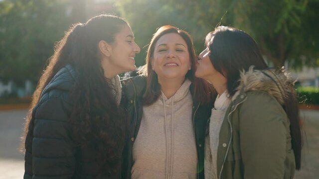 Mother and daughters kissing and hugging each other at park