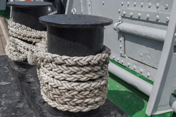 Salted, with traces of water, a black double metal posts with a stretched thick ship cable wound on it, fixed on the deck along the riveted side of the vessel.