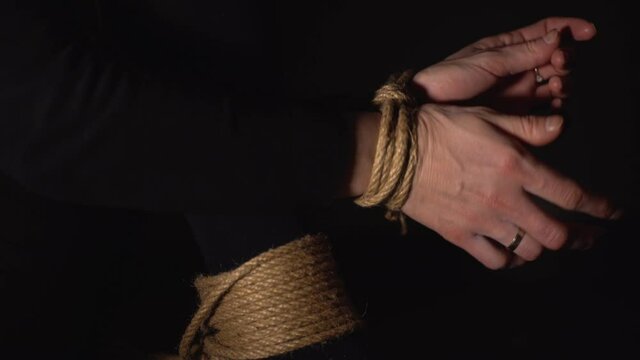 Woman is trying to free her hands and feets from rope. Human Trafficking. Domestic violence