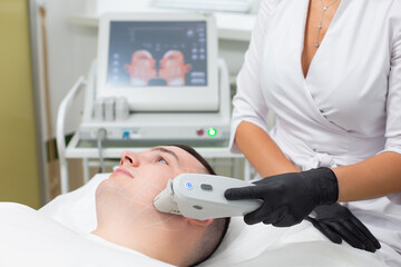 Portrait of a young man lying on the couch of a cosmetology office with marks on his face applied with a white cosmetic pencil and the hand of a cosmetologist in a medical glove performing a procedure