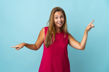 Middle age brazilian woman isolated on blue background pointing finger to the laterals and happy