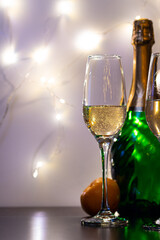 A bottle of sparkling wine, champagne glasses, with sharpness on the right glass, and tangerines, on a dark base and with a light background, in a cold key. Bright, joyful holiday atmosphere.