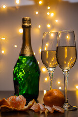 Peeled tangerine, a bottle of champagne, champagne glasses and garland bokeh. Attributes of the new year and Christmas. Merry Christmas and Happy New Year.