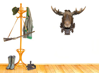 The equipment of hunter in a room with the head of reindeer as trophy on a white wall.