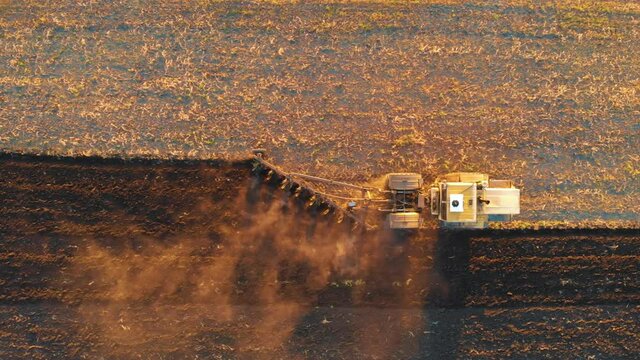 Agricultural Industry. Aerial view tractor with plough working on a field at sunset. Tractor plowing fields with a rotary plow on a large scale vegetable farm. Agriculture from above.