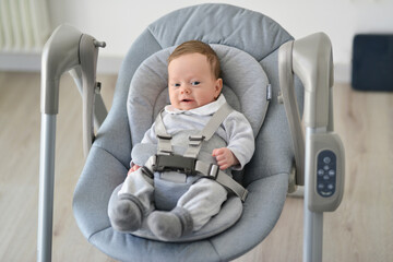 Newborn swing baby swing automatic electric chair. Cute smiling baby laying in bouncer chair. Child relaxing in a swing. Family morning at home.