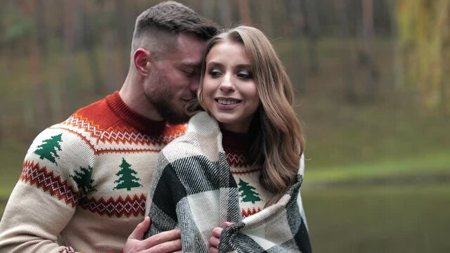 Man hugging his girlfriend in plaid standing behind her. Romantic date in the countryside near the river. Lovely couple at the backdrop of autumn nature.