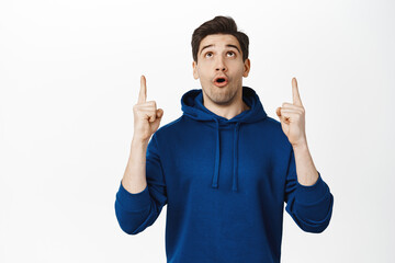 Image of amazed young man pointing and looking up, showing advertisement and gasping impressed,...
