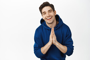Happy handsome young man smiling, showing thank you namaste gesture and laughing, express gratitude, standing over white background - obrazy, fototapety, plakaty