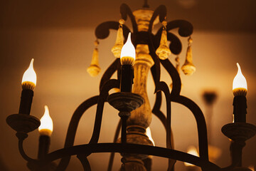 On an old elegant beautiful chandelier, lamps in the form of candles emit a bright cozy light  in the evening. A hotel or a palace. Electricity.