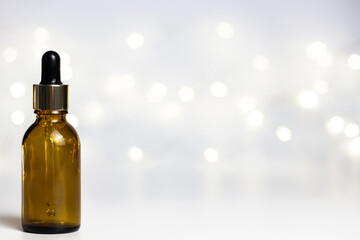 White background with warm yellow round bokeh. Copyspace. New Year's holiday lights. Christmas. Glass brown cosmetic jars with a pipette. Artificial Christmas tree.